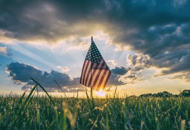 An american flag is sitting in the middle of a grassy field at sunset.