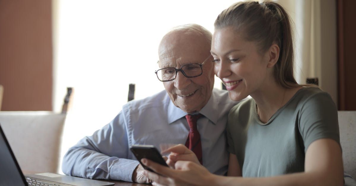 An elderly man and a young woman are looking at a cell phone together.