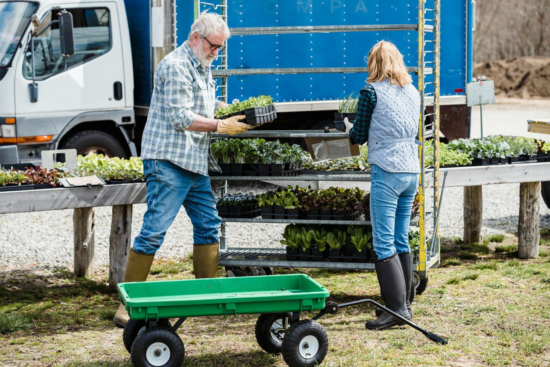 A man is pushing a green wagon next to a woman.
