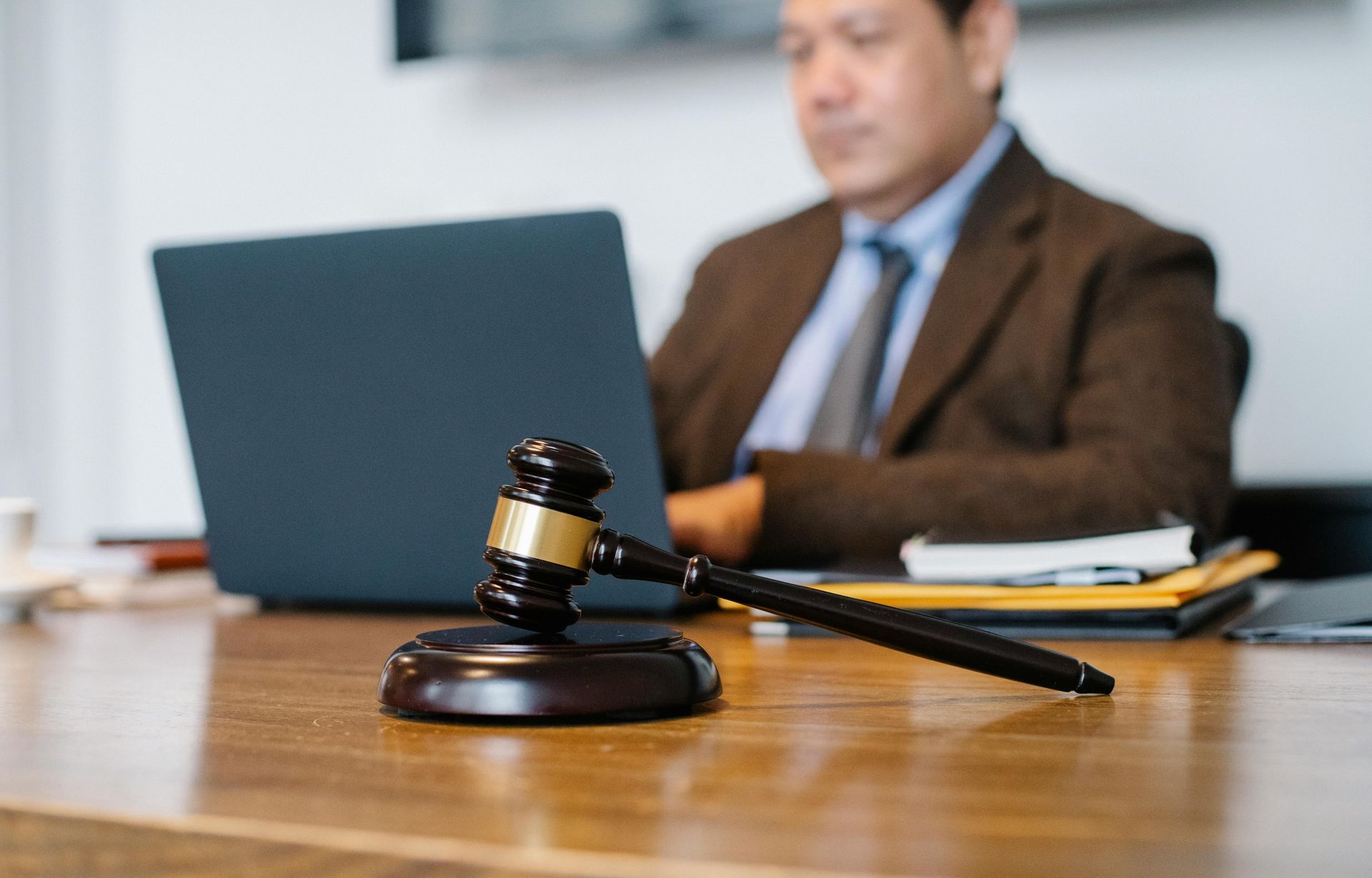 A judge 's gavel is sitting on a wooden table next to a man using a laptop.