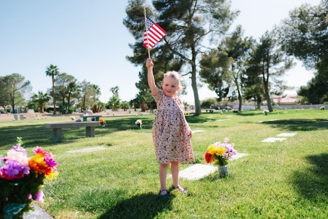 A little girl is holding an american flag in a cemetery.