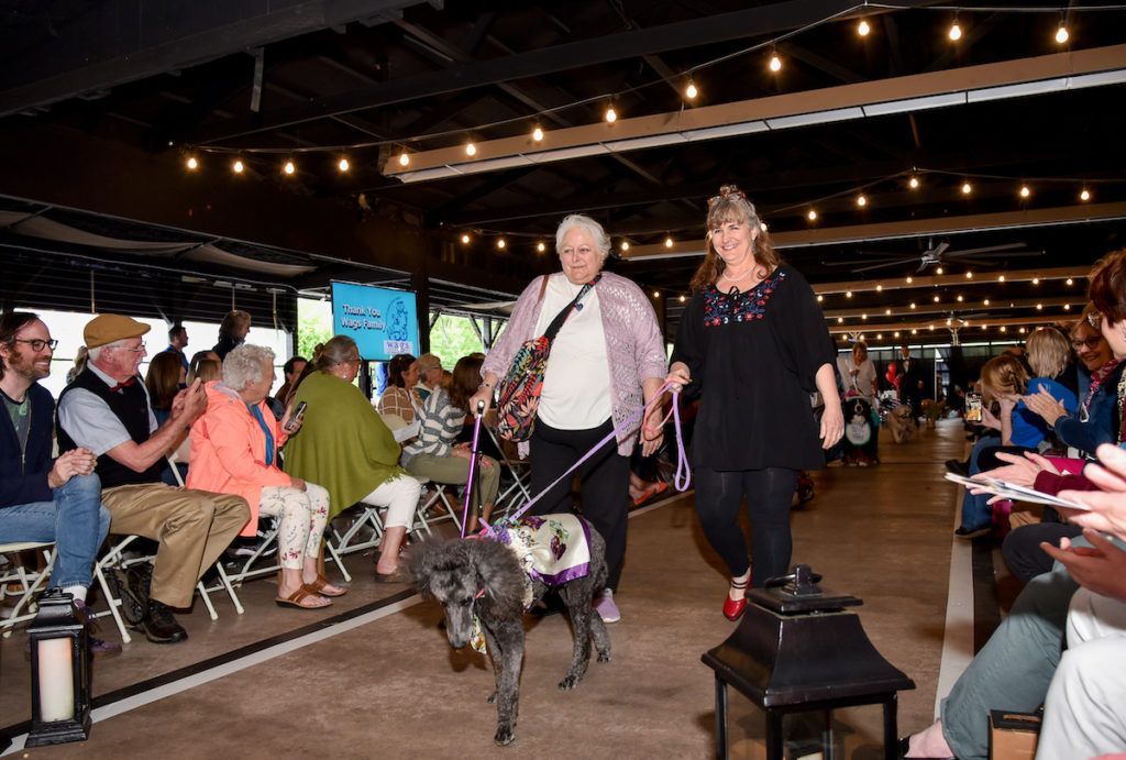 A woman is walking a dog on a leash in a park.