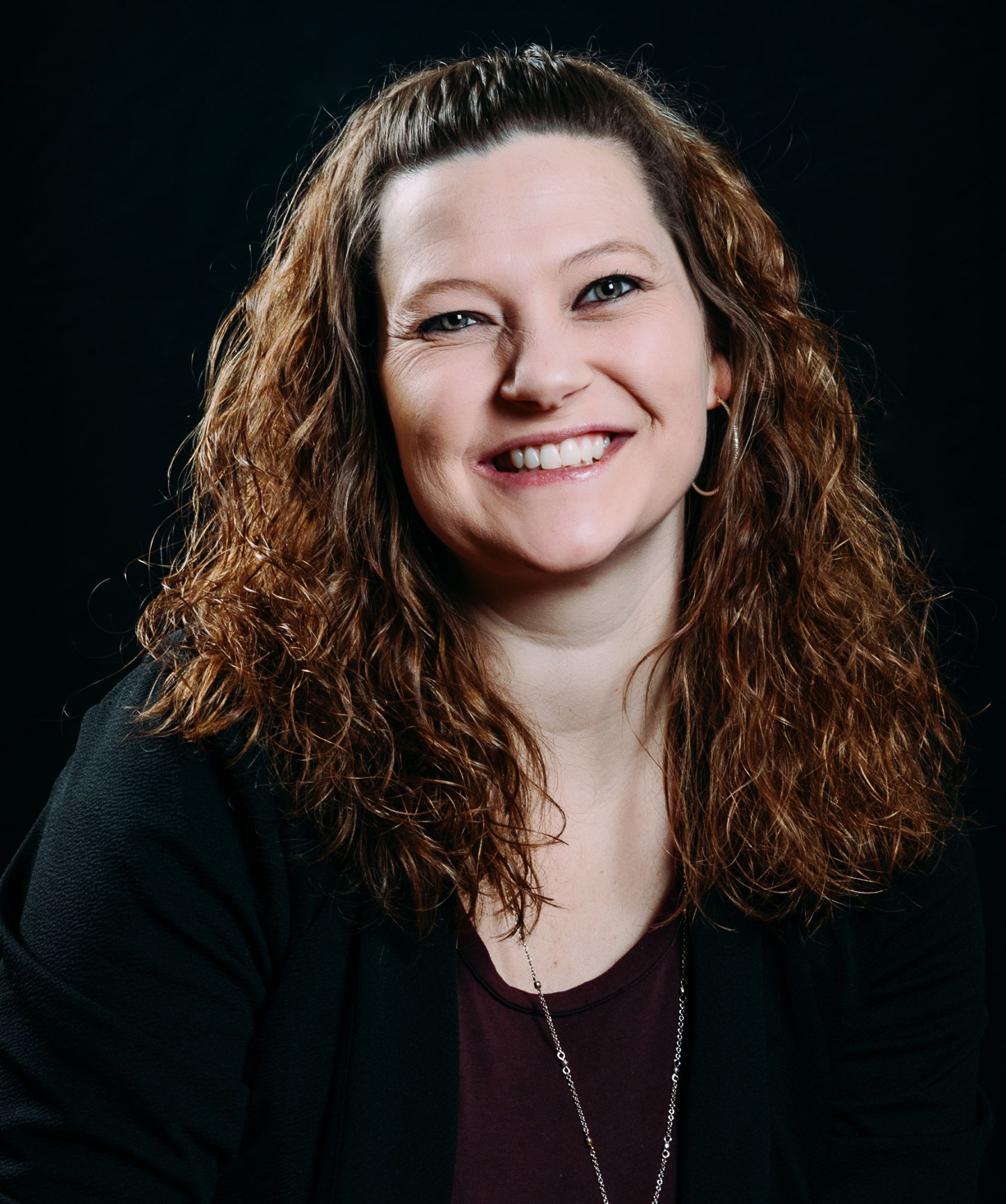 A woman with long curly hair is smiling for the camera.