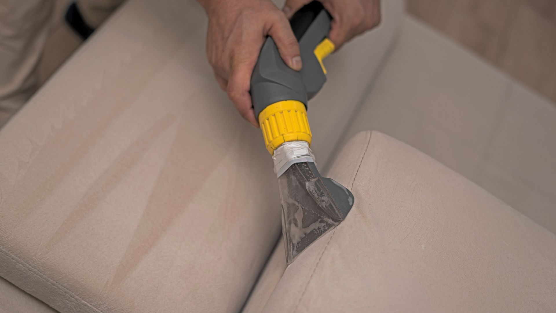 A person is cleaning a couch with a vacuum cleaner.
