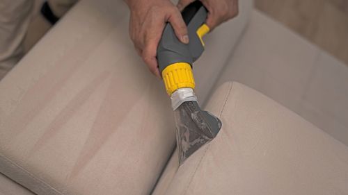 A person is cleaning a couch with a vacuum cleaner.