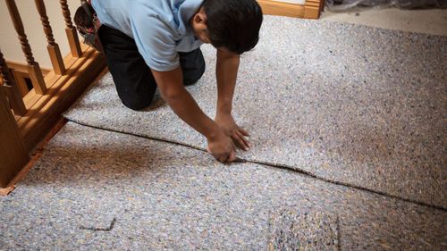A man is kneeling on the floor cutting a piece of carpet.