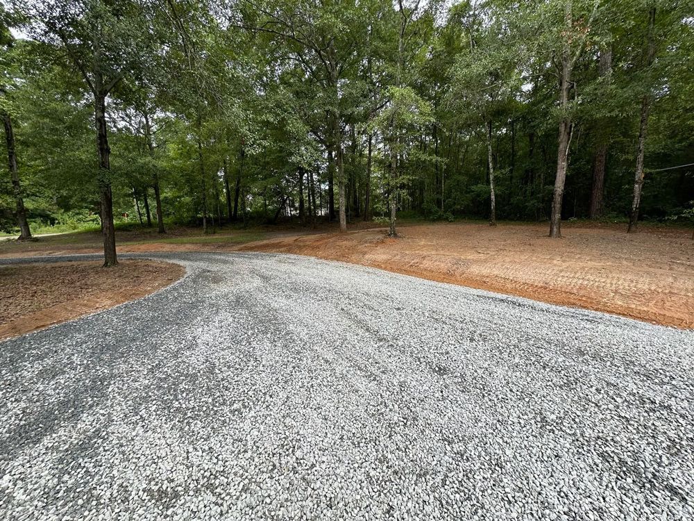 A gravel road going through a forest with trees on both sides.