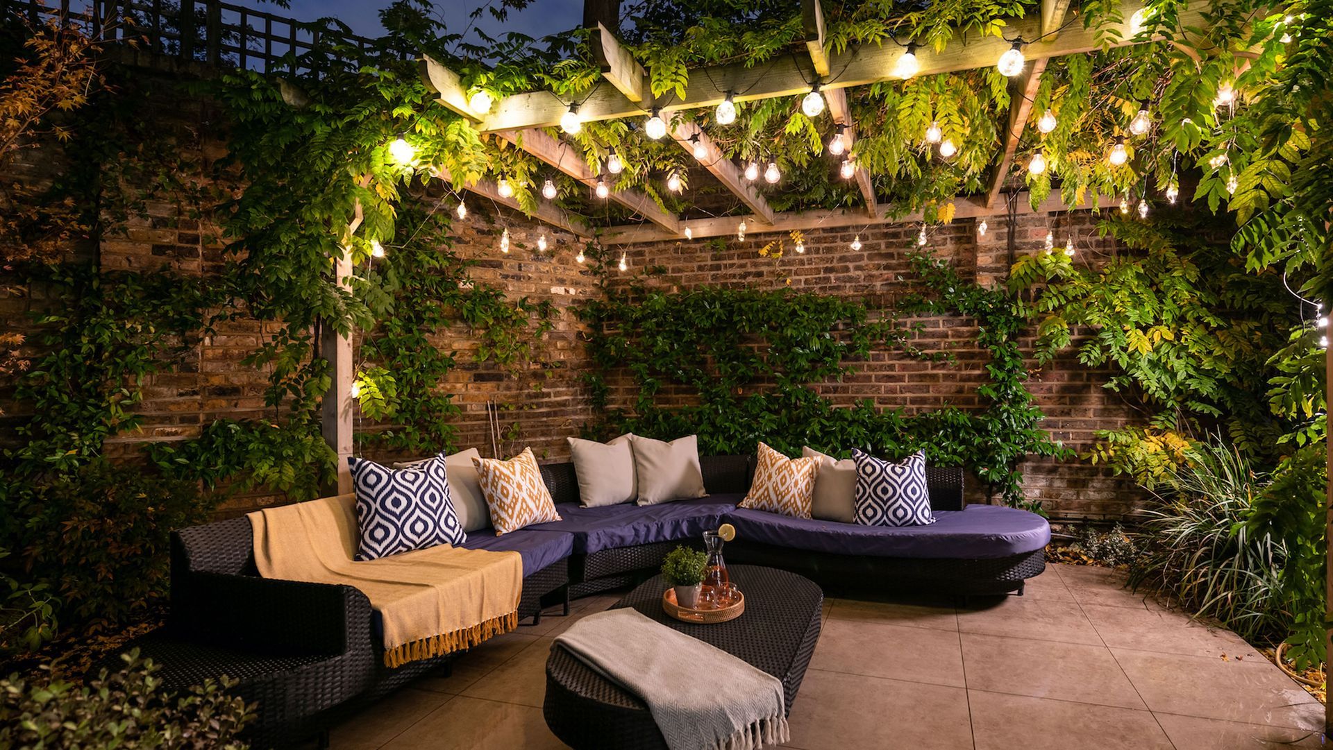 Cozy outdoor seating area at night, with string lights and climbing plants.