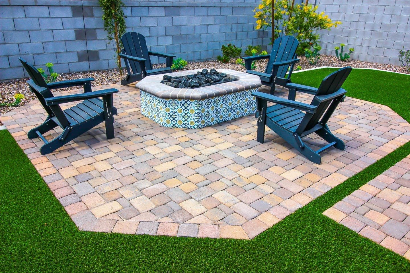 Patio with a fire pit surrounded by Adirondack chairs, brick pavers, and green turf.
