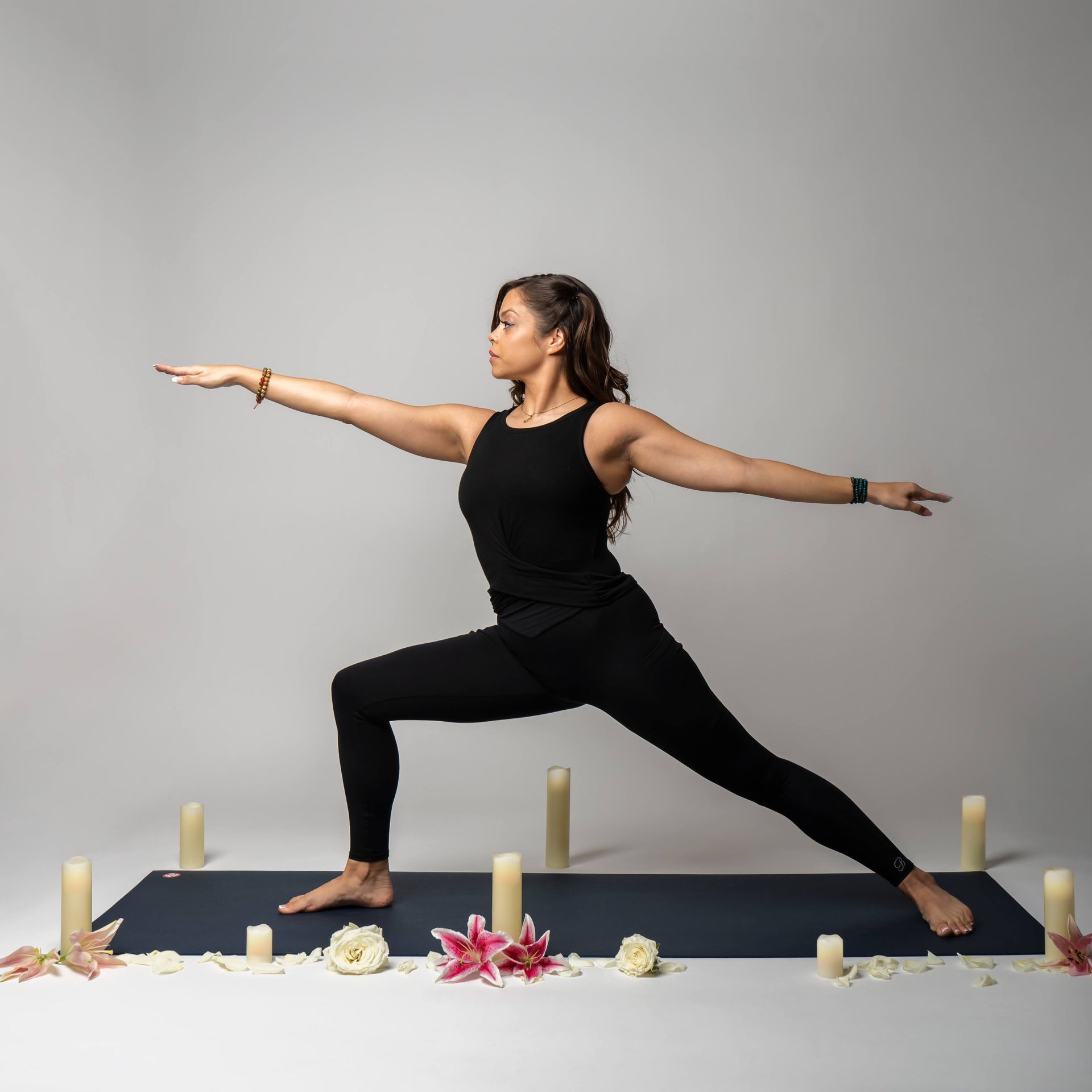 A woman is doing a yoga pose on a mat surrounded by candles and flowers.