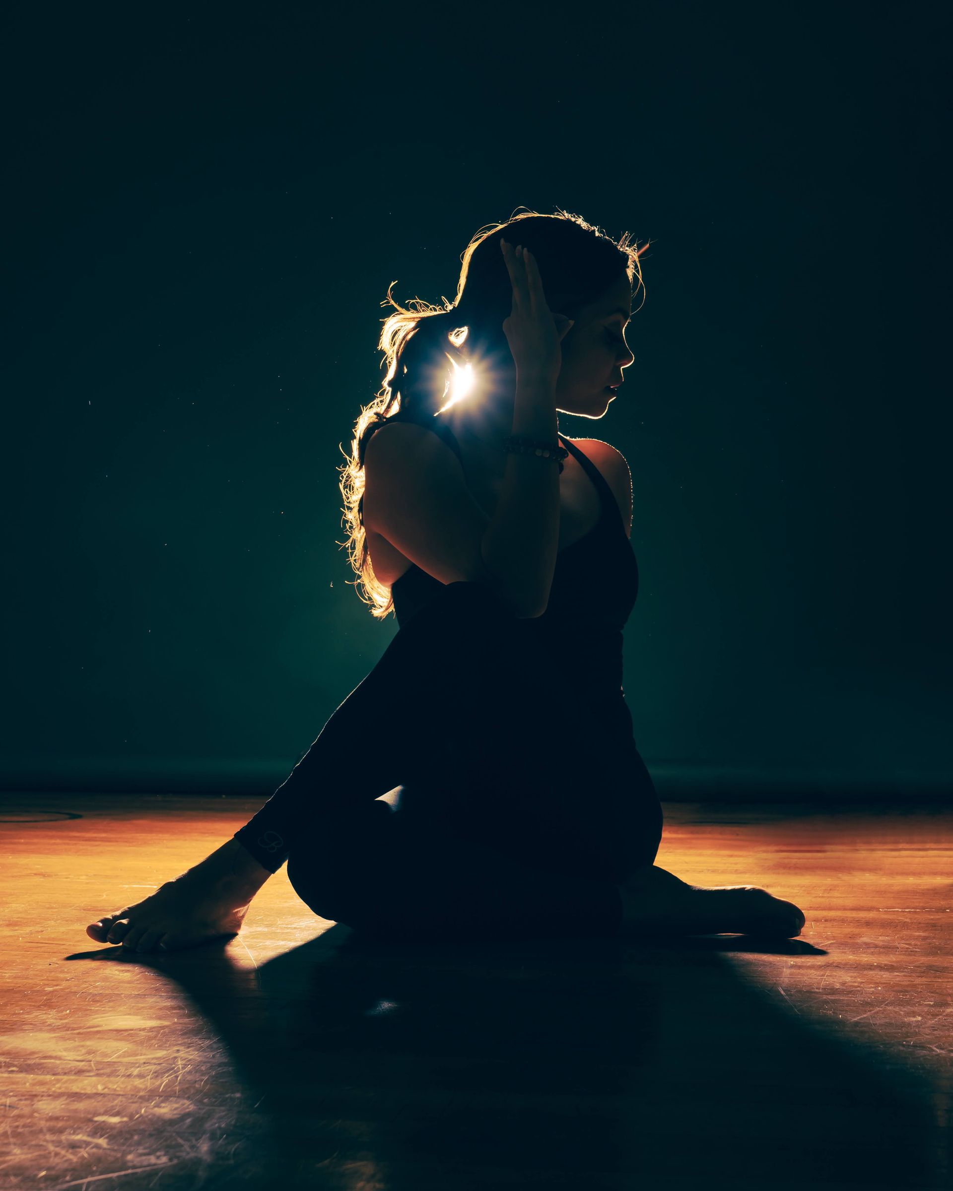 A silhouette of a woman sitting on the floor in a dark room.