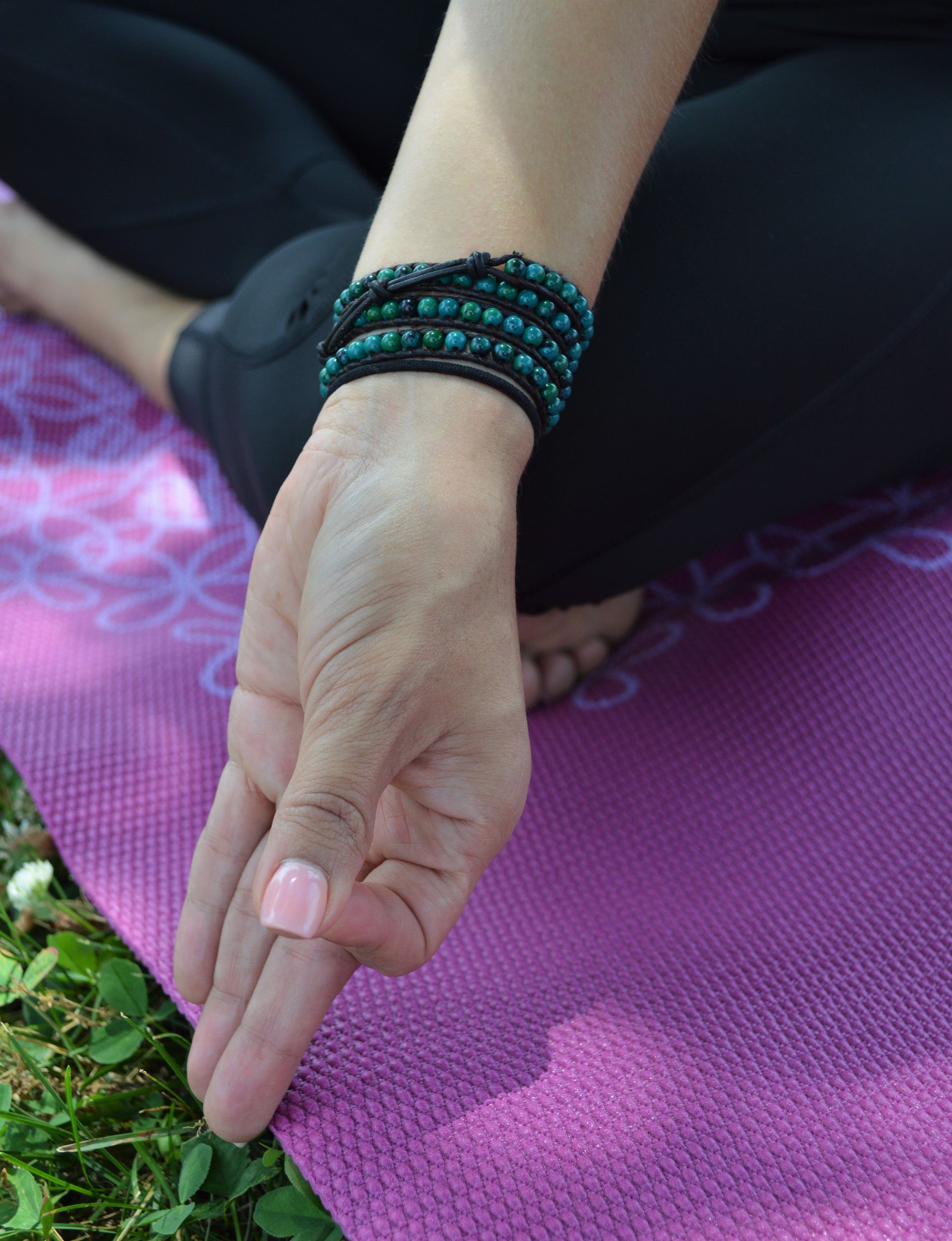 A woman is sitting on a pink yoga mat and touching a plant with her finger.