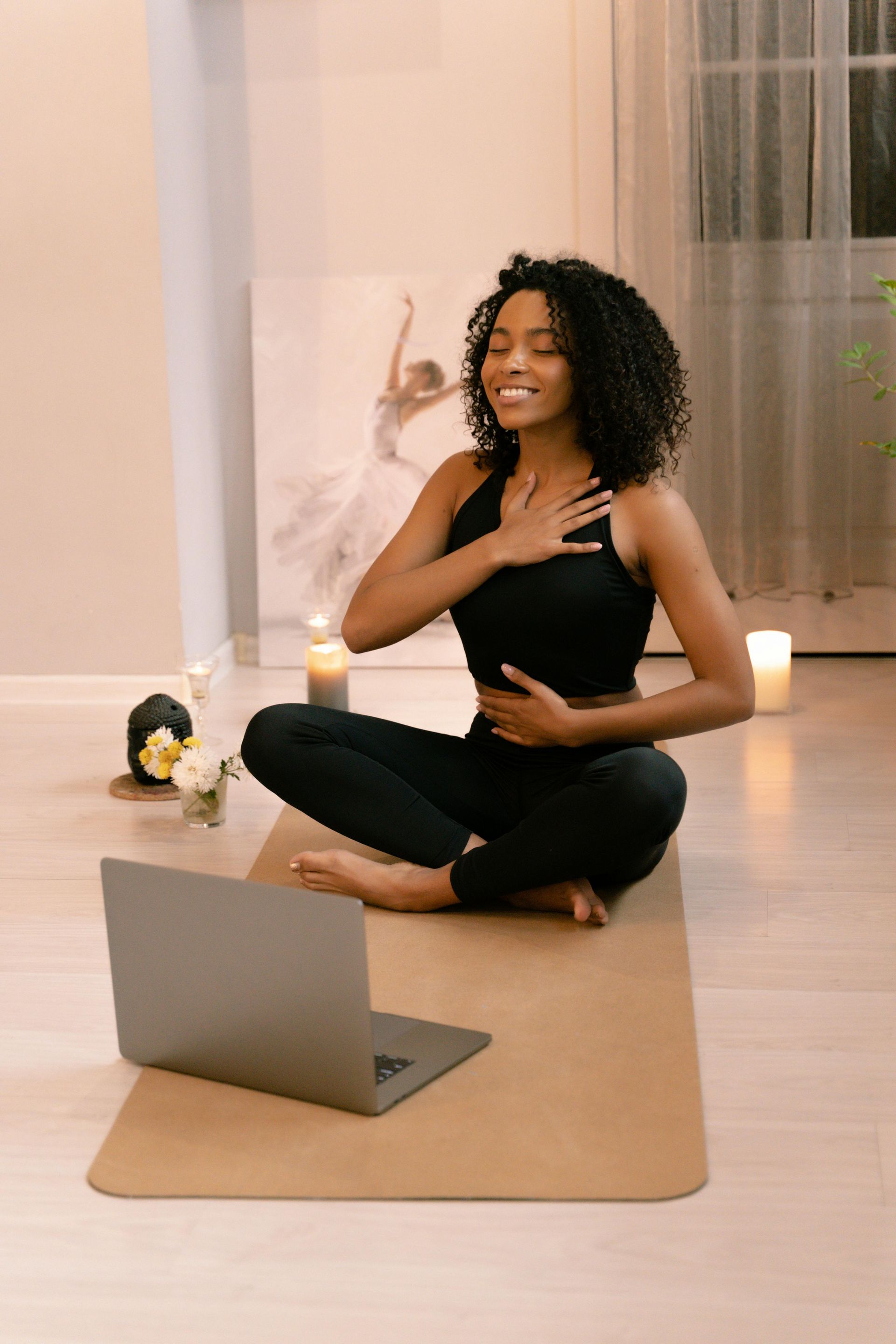 A woman is sitting on a yoga mat in front of a laptop computer.