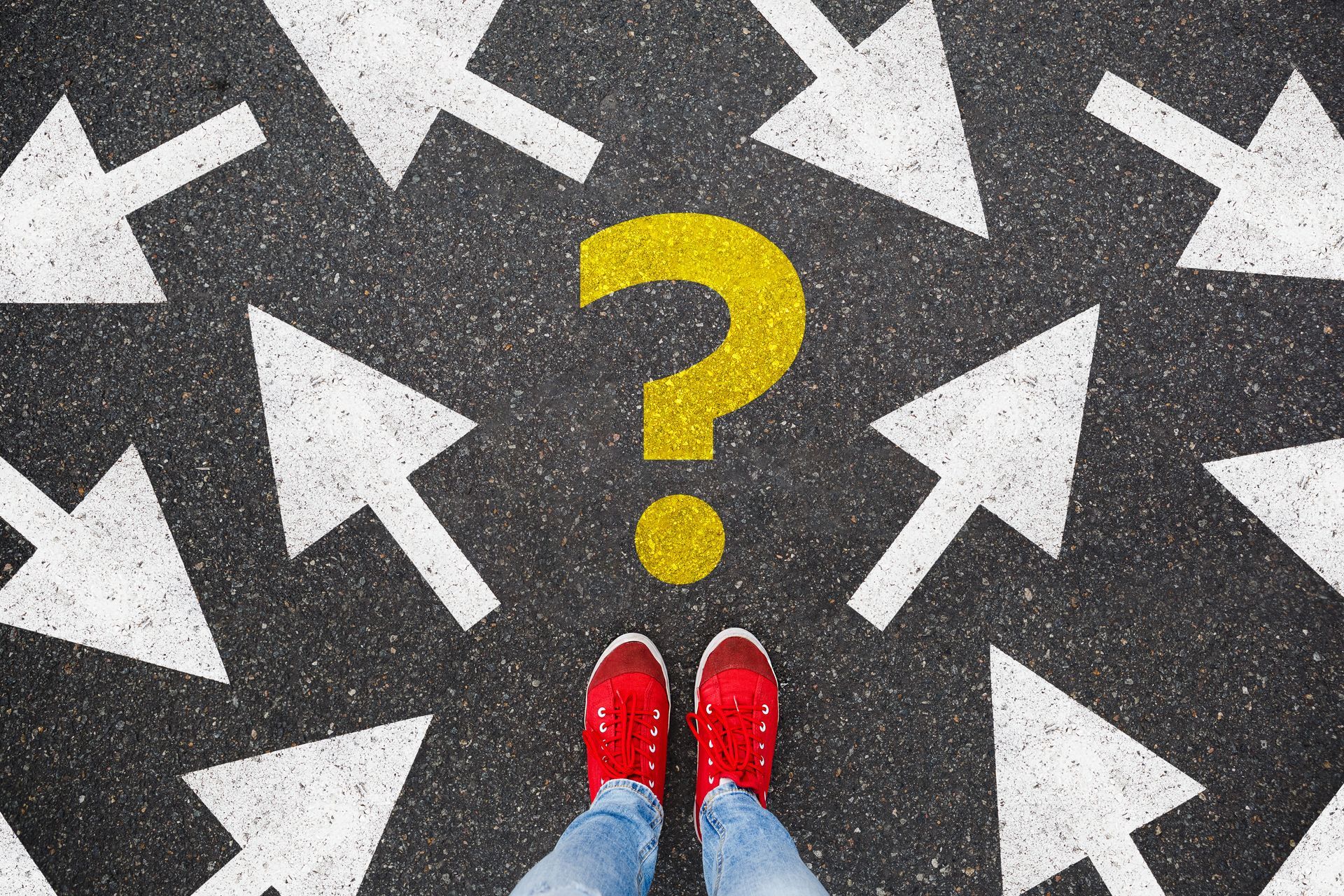 Red sneakers on asphalt with question mark surrounded by white arrows pointing in different directions.