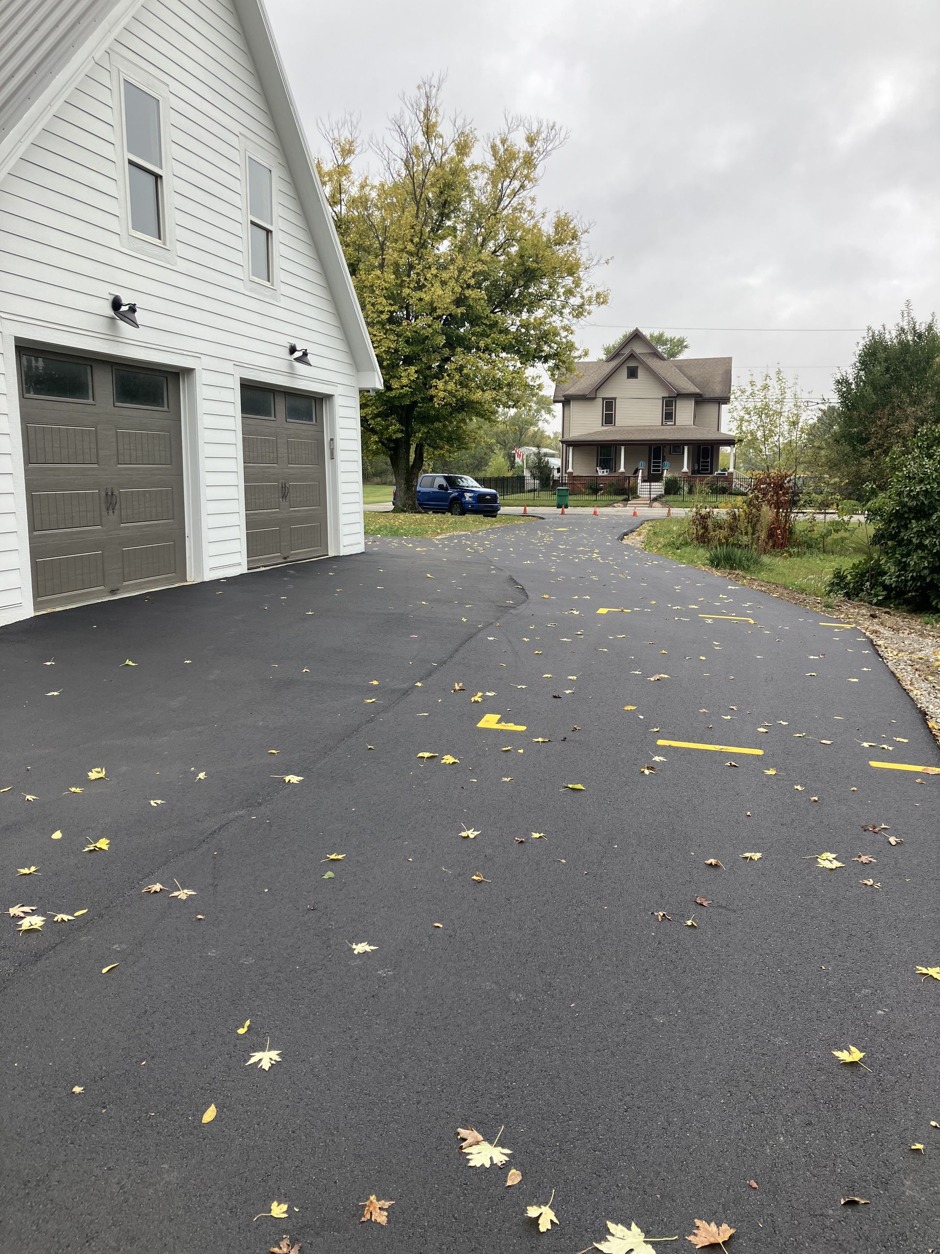 Asphalt driveway leads to a two-car garage on a cloudy day; a house is in the background.