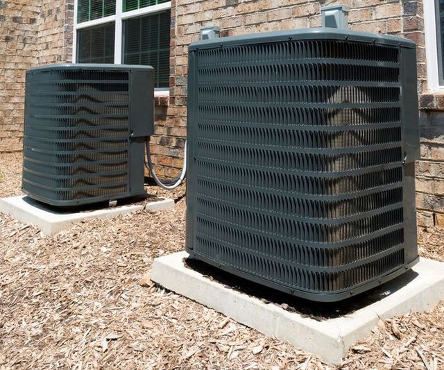 Two outdoor HVAC units on concrete pads beside a brick building