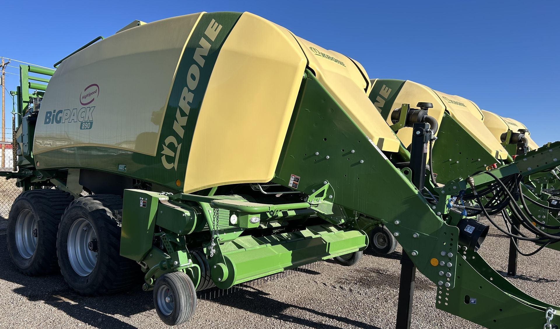 A row of yellow and green Krone BiG Pack agricultural balers parked on a gravel lot under a clear blue sky.