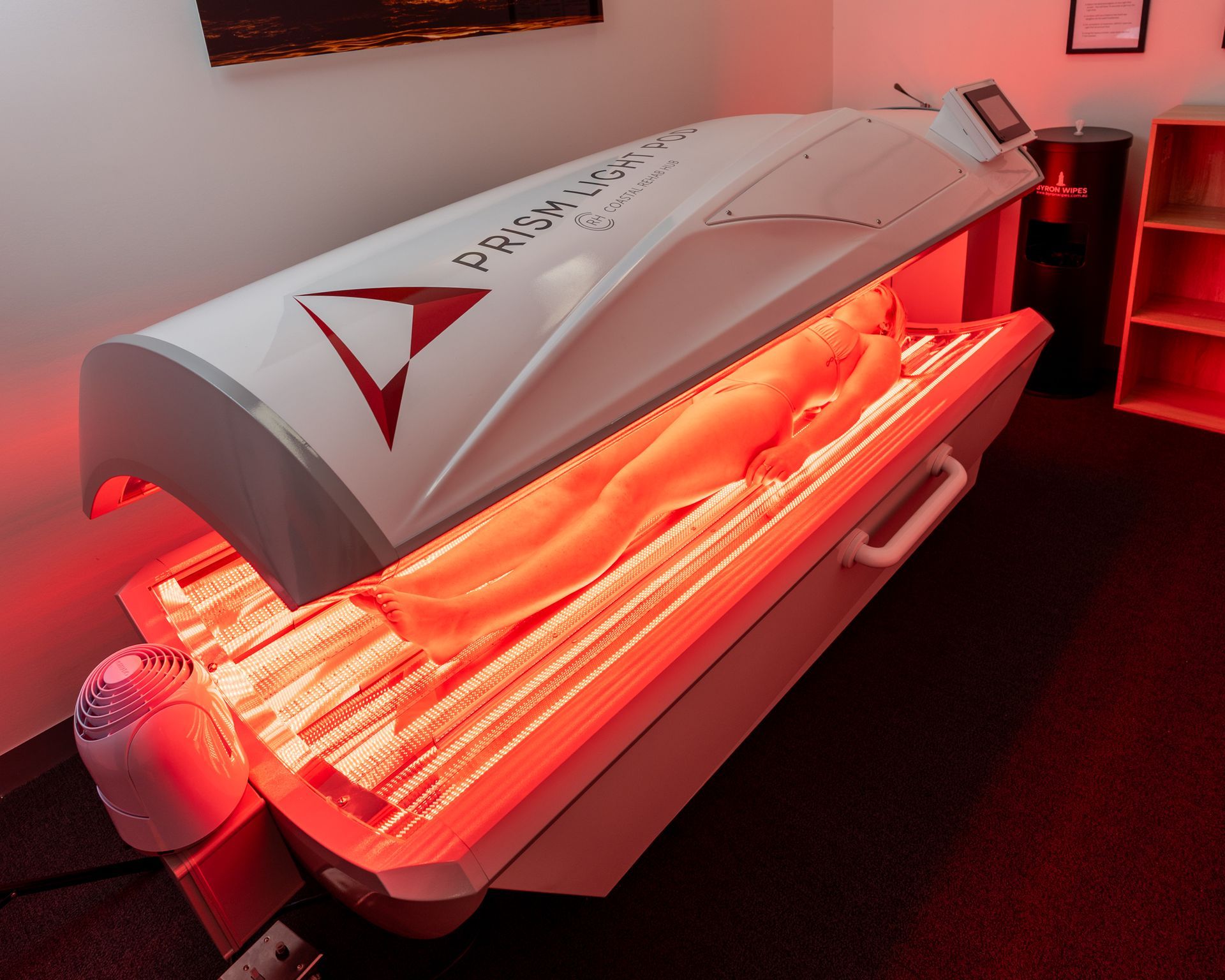 Person inside a red light therapy bed; white and red device, red glow.