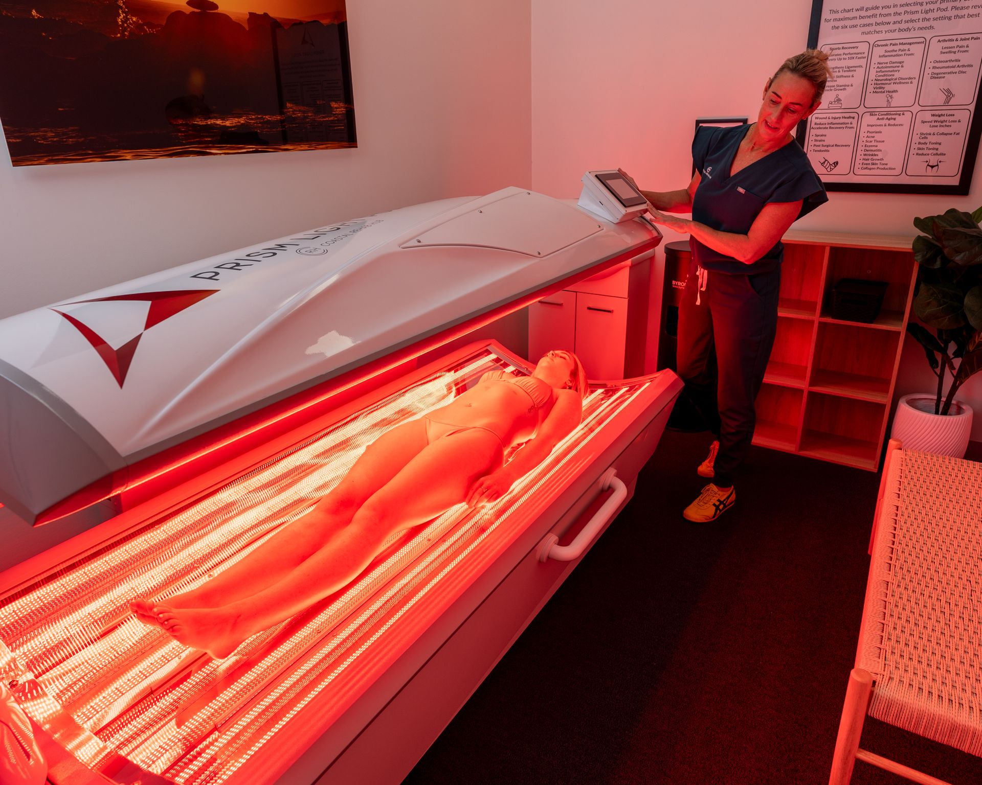 A woman operating a red light therapy machine. A person is lying inside the machine.