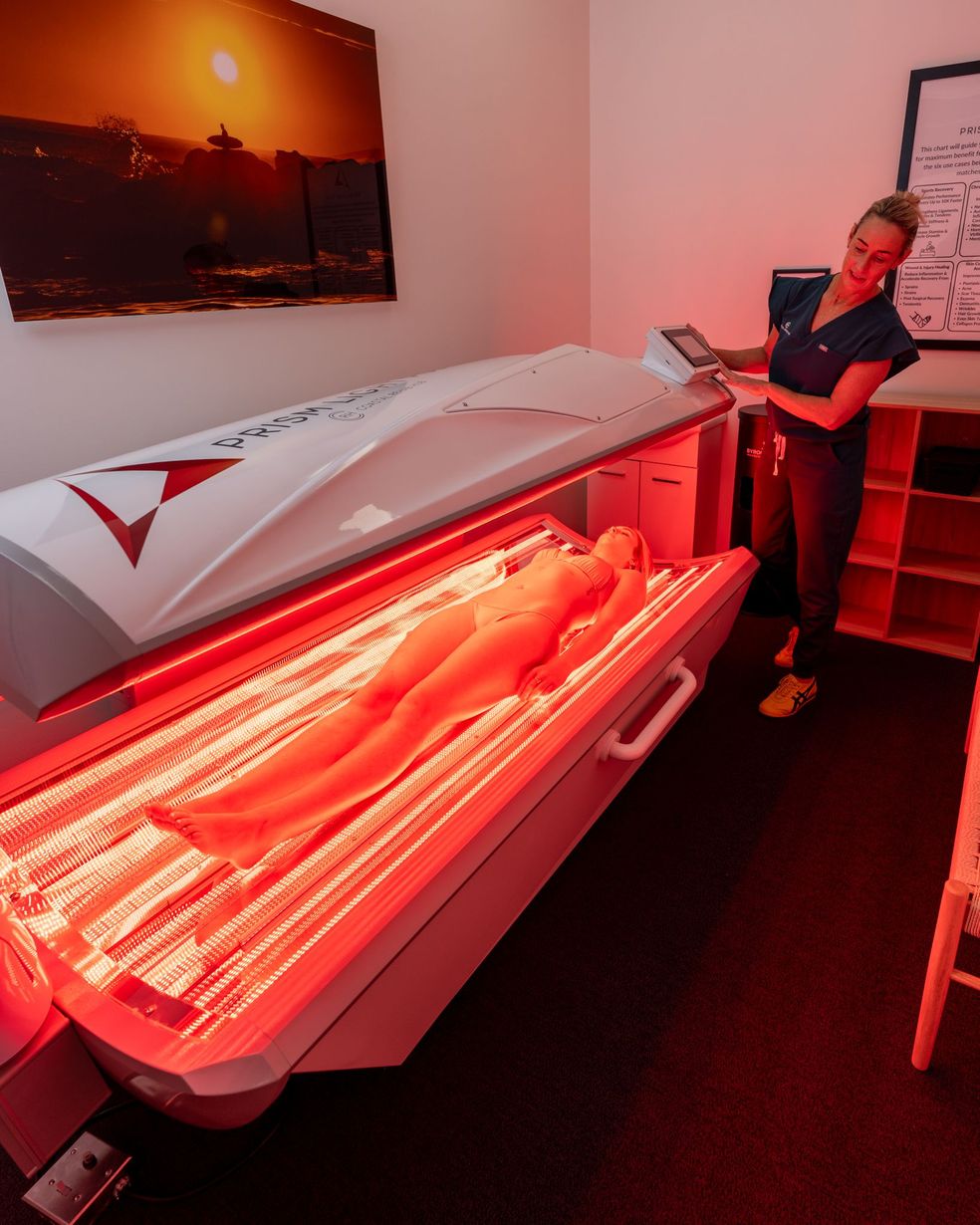Woman operating a red light therapy bed, with a person lying inside. Bright red interior.