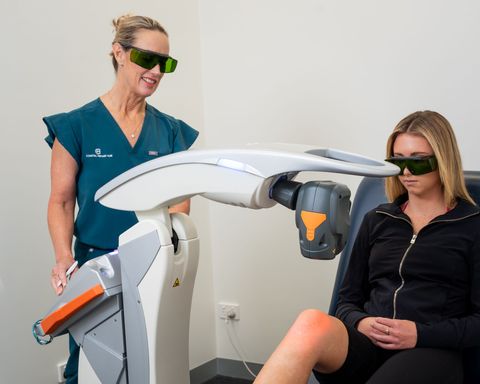 Therapist using laser treatment on patient's knee, both wearing protective eyewear in a clinic.