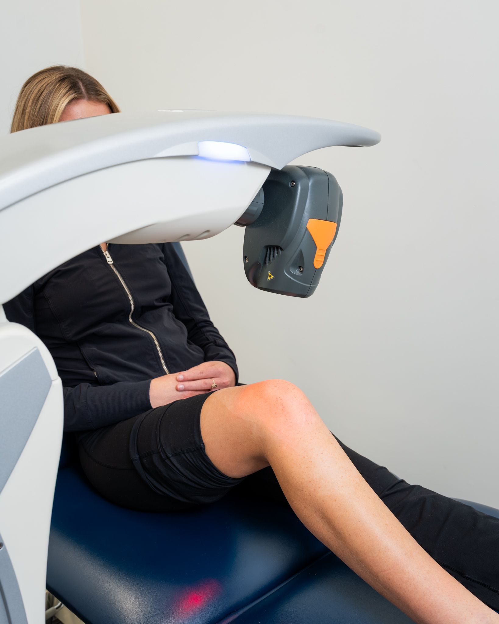 Woman undergoing knee medical treatment with laser device.