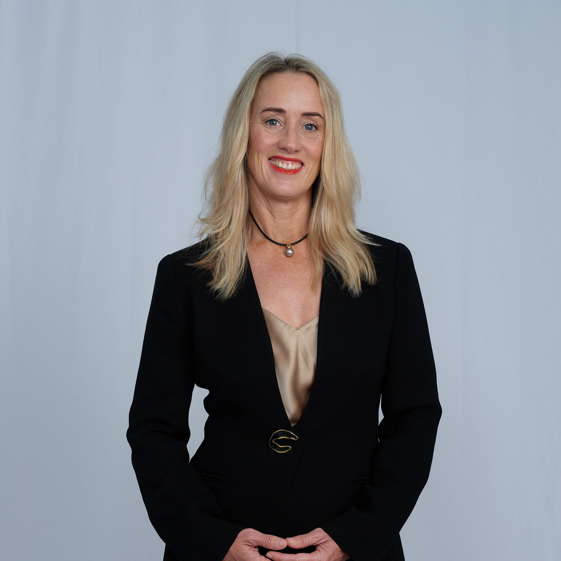 Blonde woman in pink shirt smiles. Light blue and wooden background.
