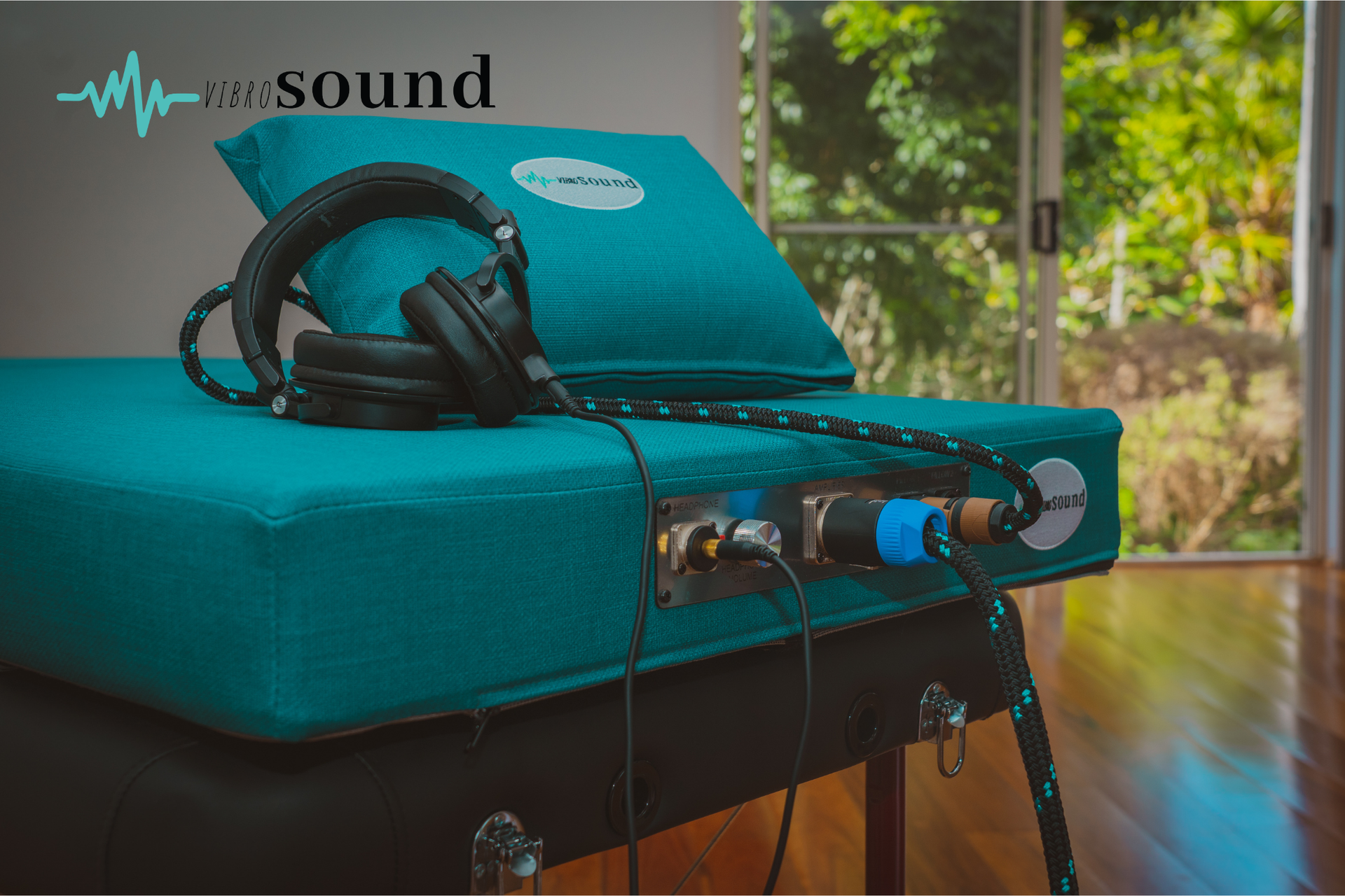 Woman reclining on a couch, hugging a pink pillow and wearing headphones, smiling.
