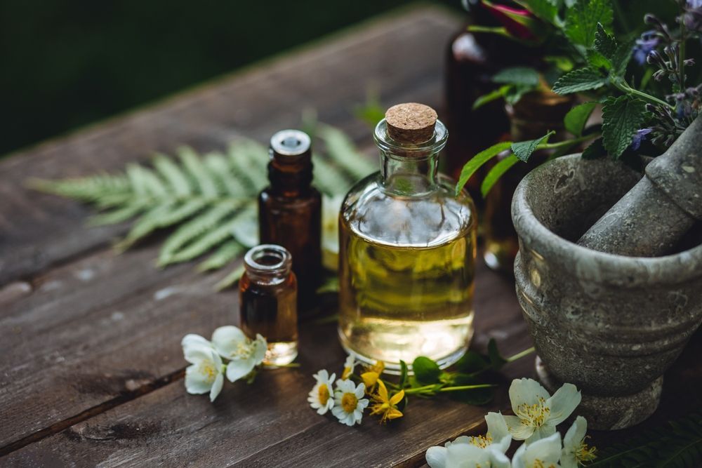 Essential oils, a mortar and pestle, and scattered flowers on a rustic wooden table.