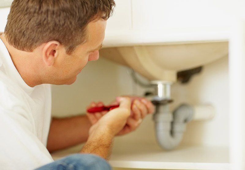 A man tightens the fittings underneath a sink.