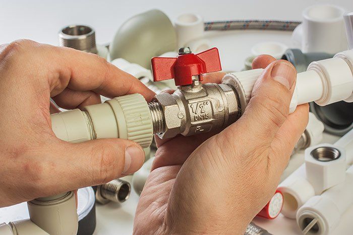 A man tightens the fittings underneath a sink.