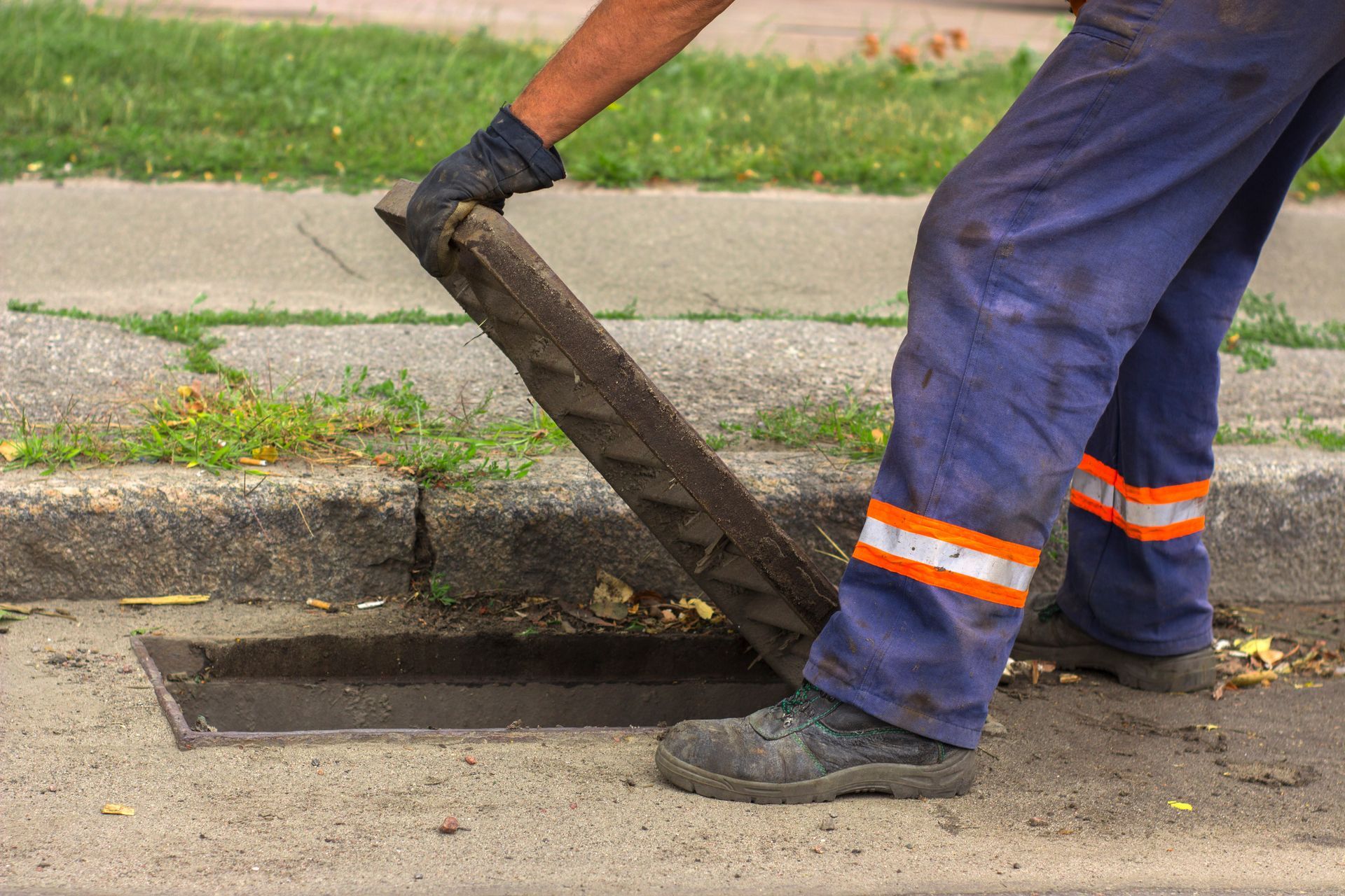 Worker lifting storm drain cover for sewer maintenance on city street.