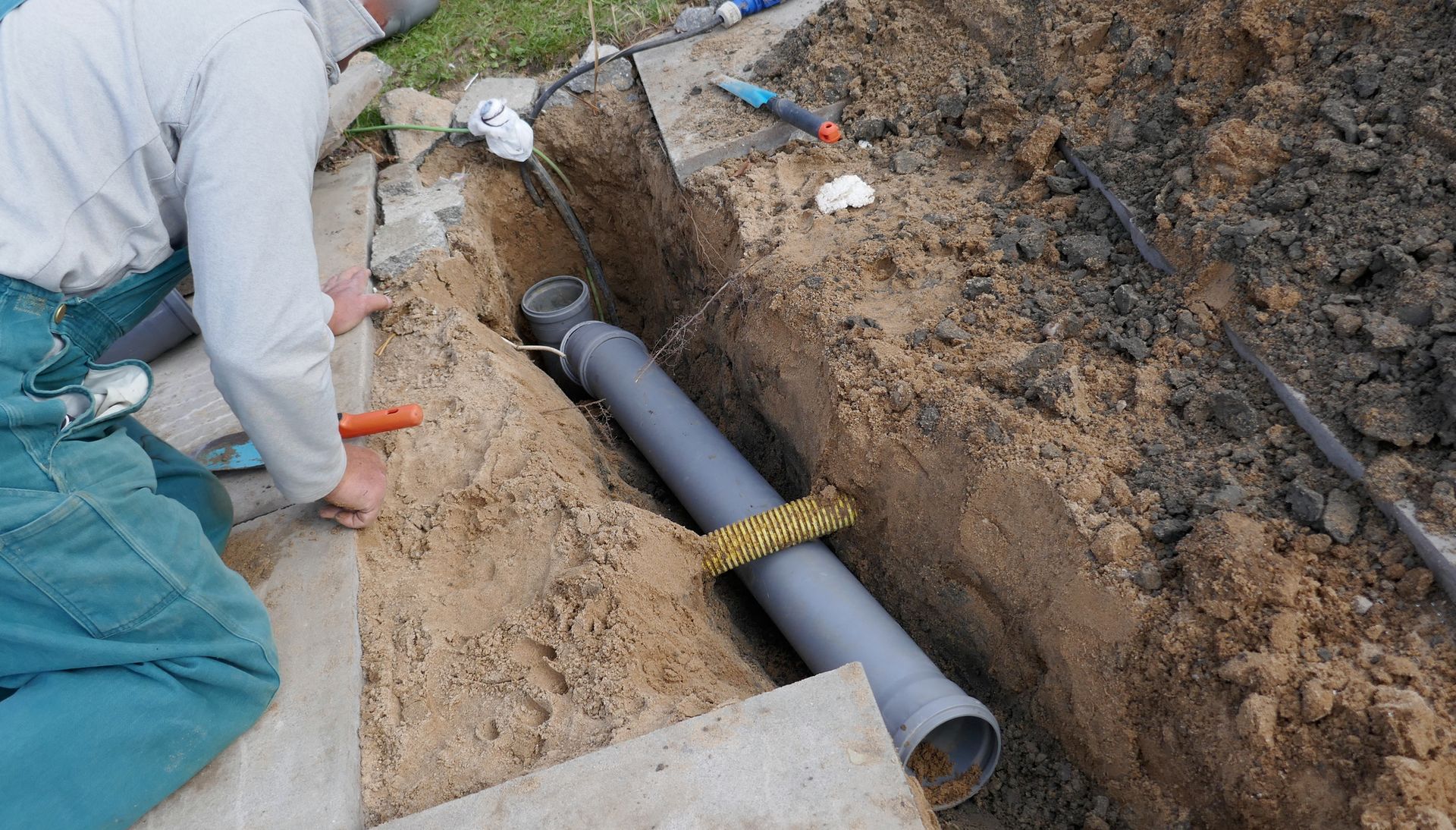 A male worker is laying a PVC pipe for a sewer line repair job.