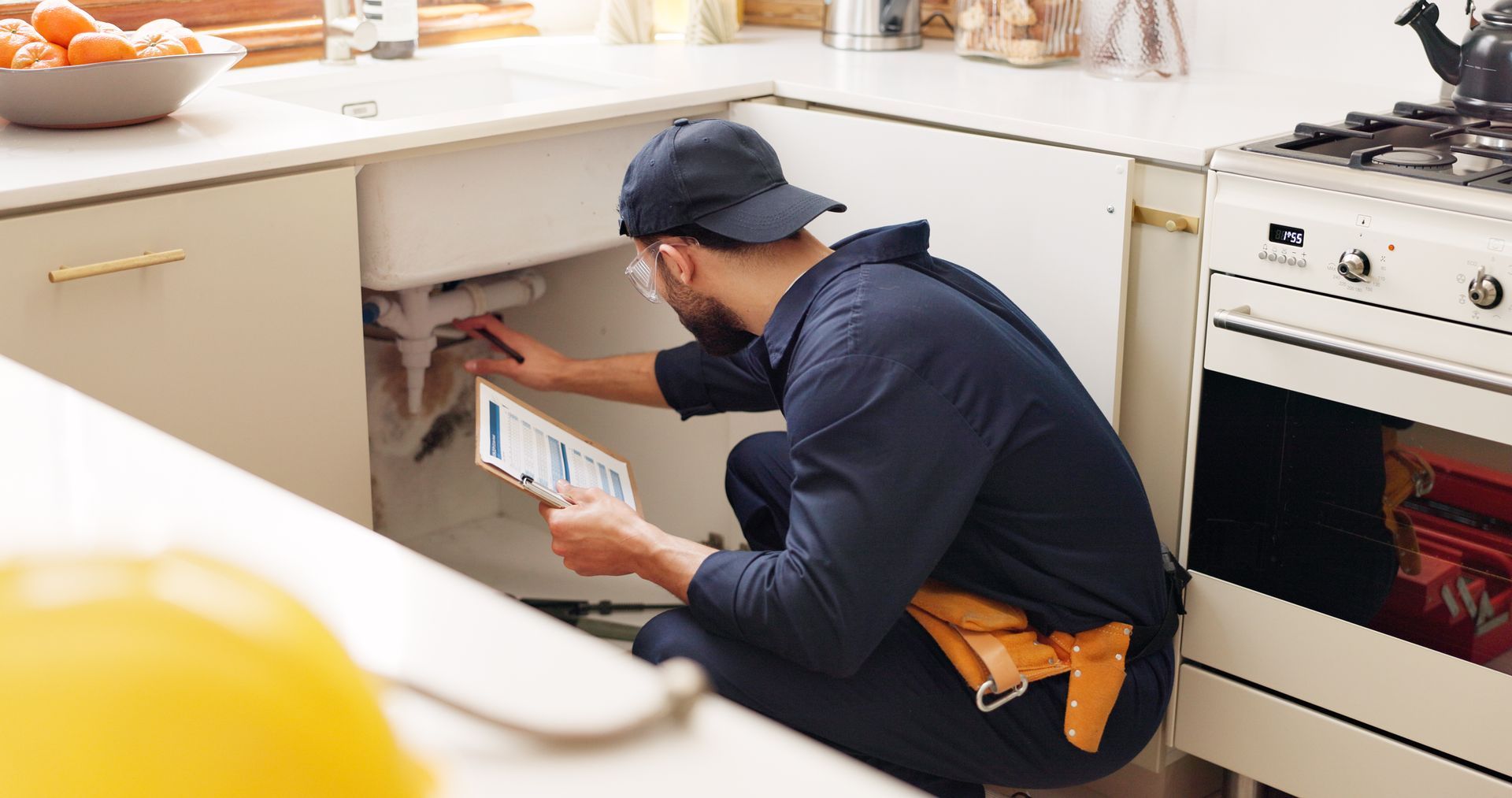Plumber fixing a kitchen sink while holding a tablet.
