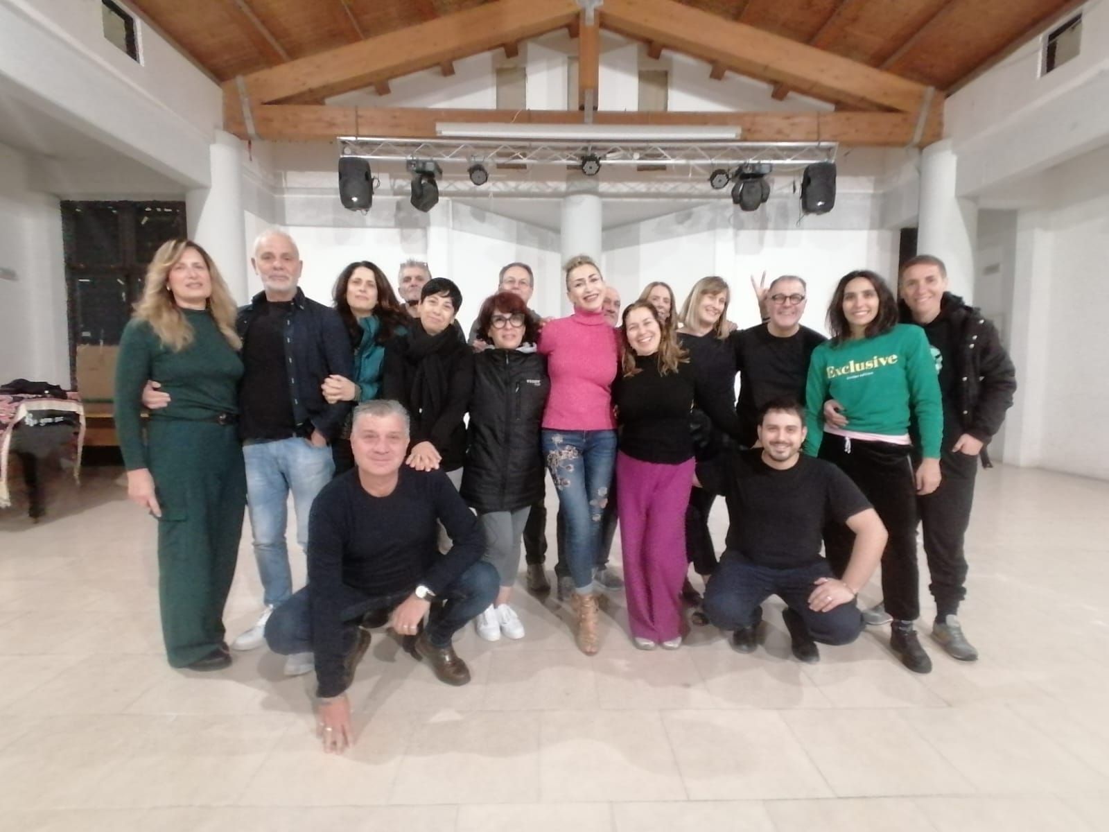 Un gruppo di persone in una grande stanza, sorridenti, posano per una foto sotto le luci del palco.