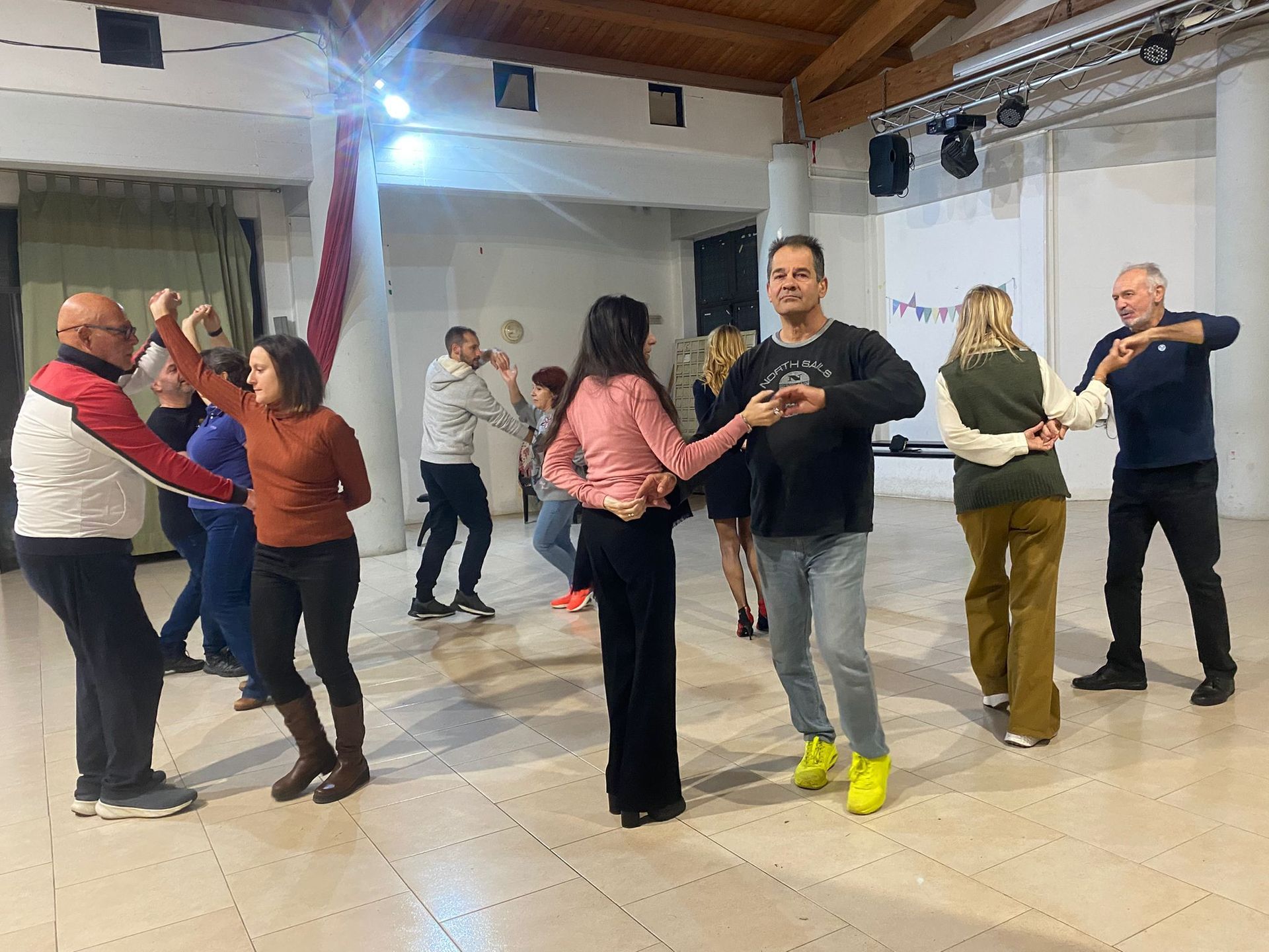 Persone che ballano in uno studio illuminato a giorno. Le coppie sono in varie pose di danza.