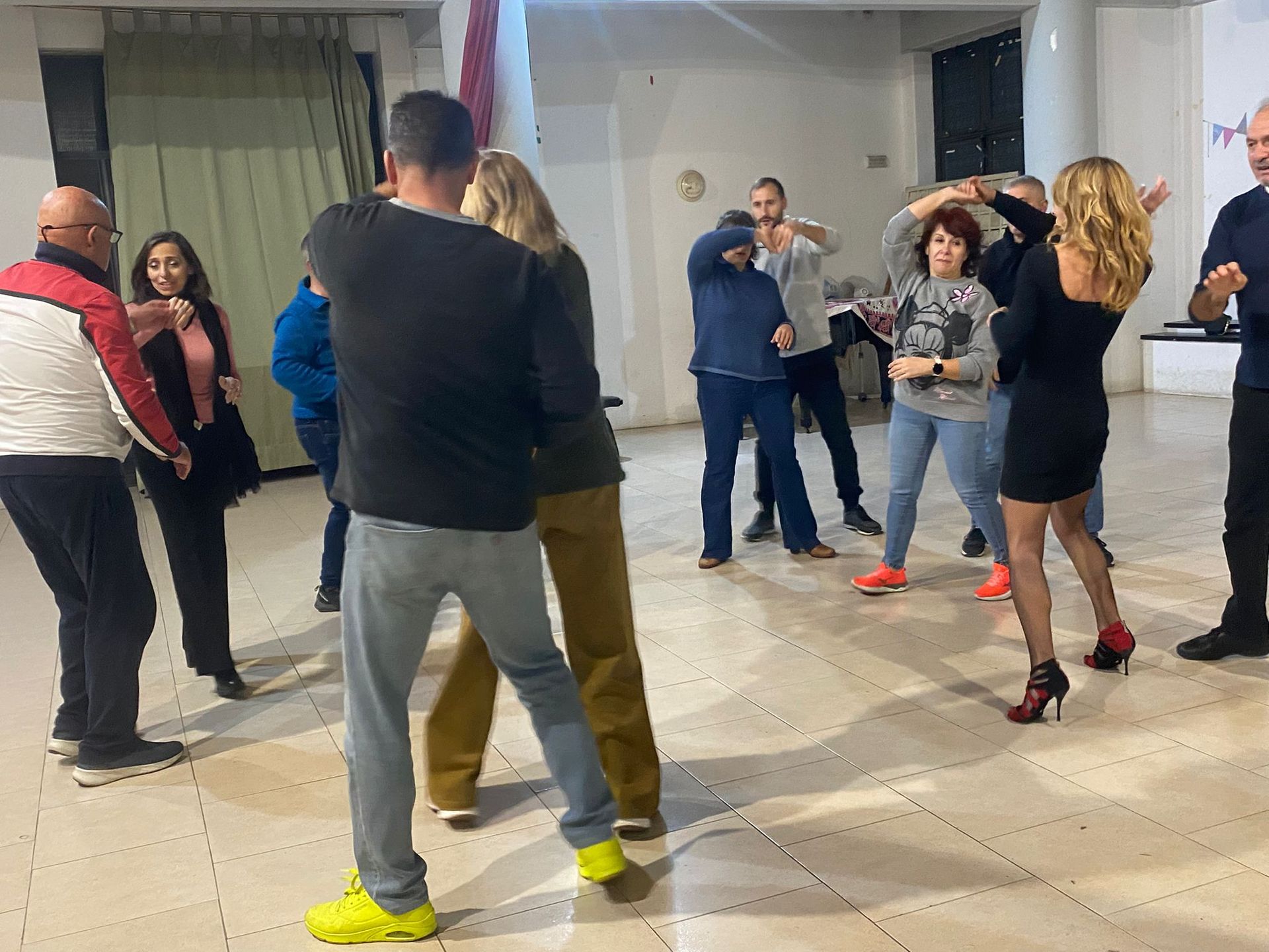 Persone che ballano in una stanza illuminata. Alcune si tengono per mano, con espressioni diverse.