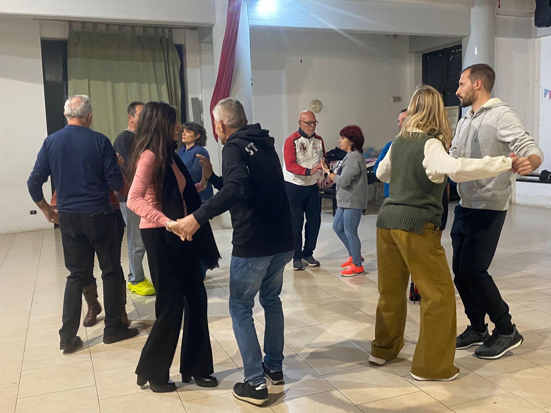 La gente balla in una stanza illuminata. Diverse coppie si tengono per mano e sorridono.