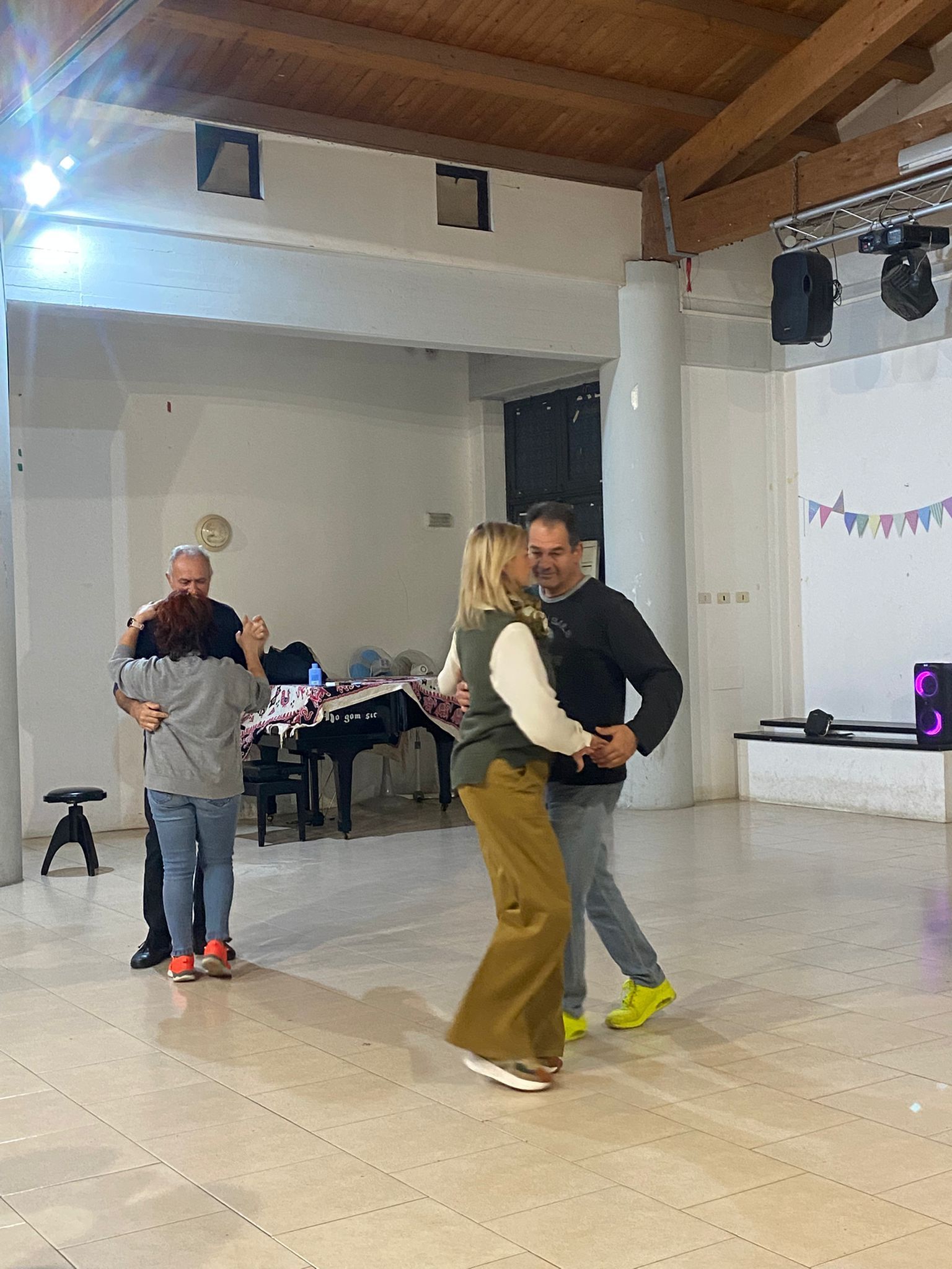 Edificio a tre piani con facciata beige e grigia, posti a sedere nel patio, grande albero, ambientazione montuosa.