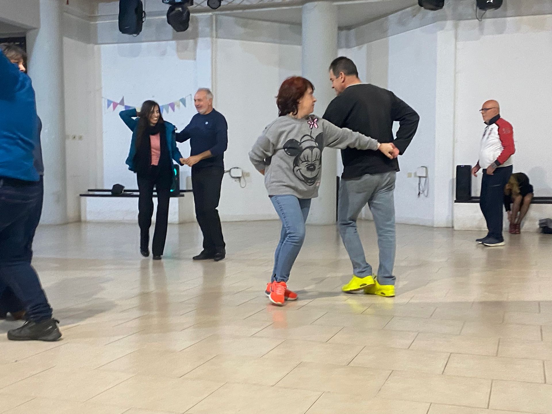 Edificio a tre piani con facciata beige e grigia, posti a sedere nel patio, grande albero, ambientazione montuosa.