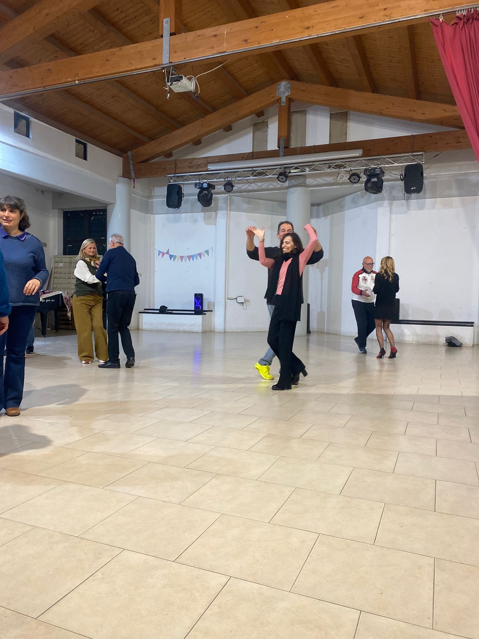 Persone che ballano in una spaziosa sala con travi in ​​legno. Una persona alza le braccia in segno di eccitazione.