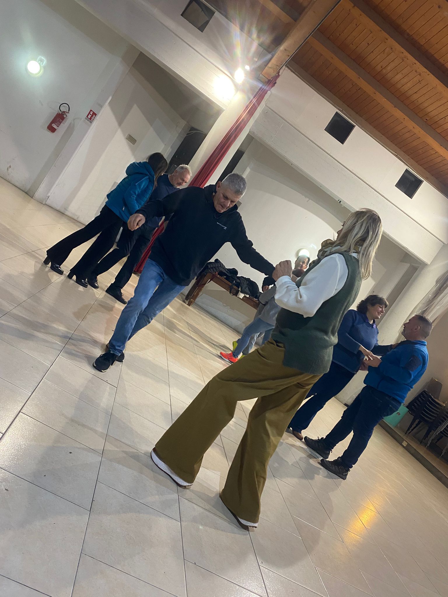 Persone che ballano in una stanza ben illuminata, con un pavimento piastrellato e una colonna rossa e bianca.