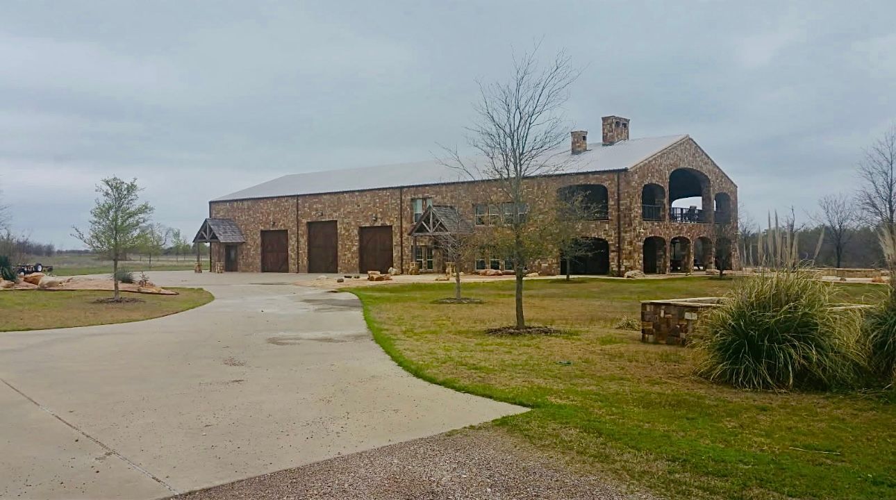 Stone building with arched windows and garage doors, on a grassy lot, under a cloudy sky.