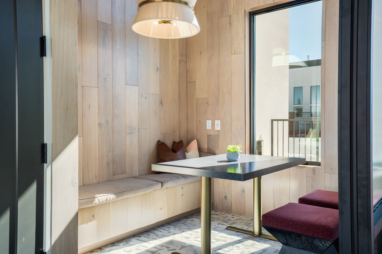 Interior dining nook with wood-paneled walls, built-in bench seating, and a square table by a large window.