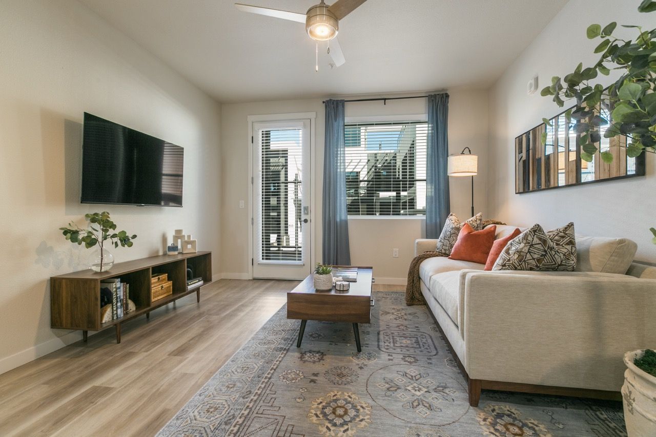 Light-filled living room in a modern apartment with a beige sofa, coffee table, and wall-mounted TV.