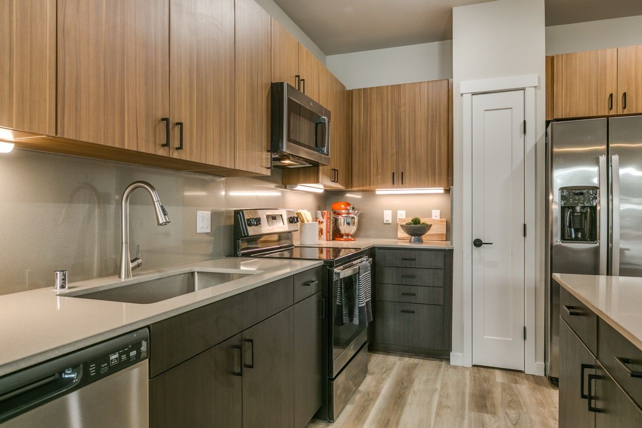 Modern kitchen with wood upper cabinets, dark lower cabinets, and stainless steel appliances.