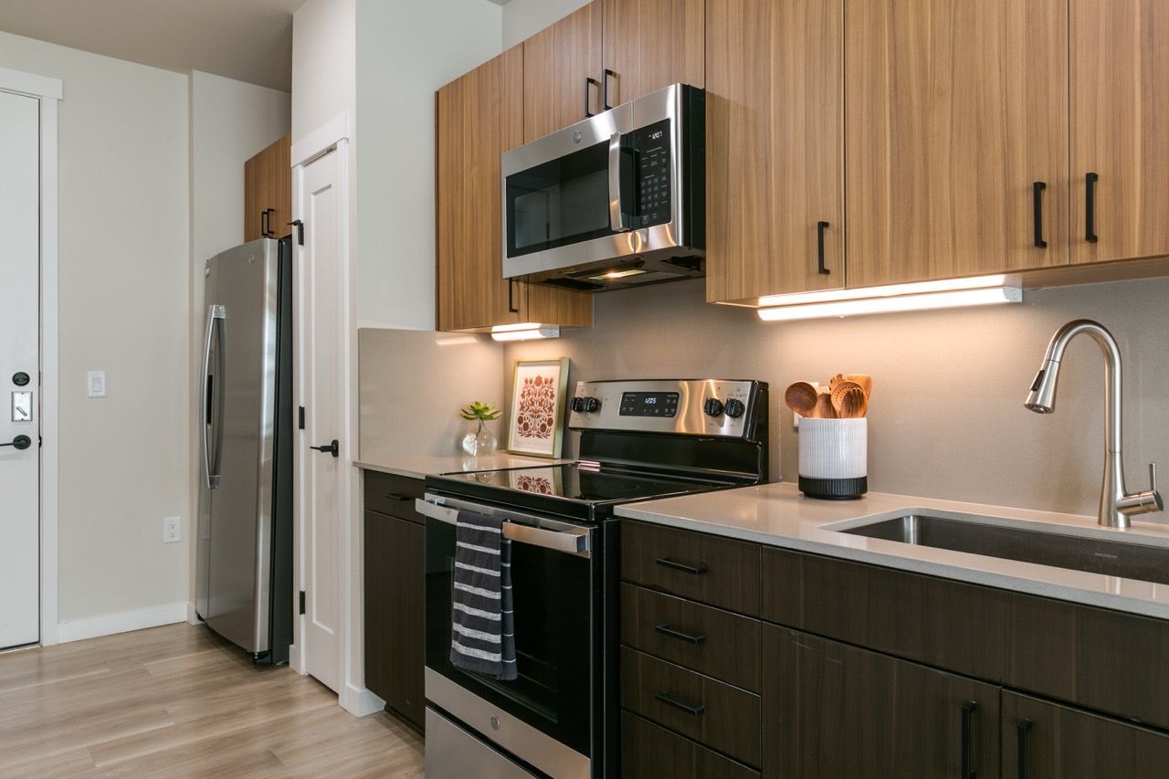 Modern apartment kitchen with stainless steel fridge, oven, microwave, and dark wood cabinets.