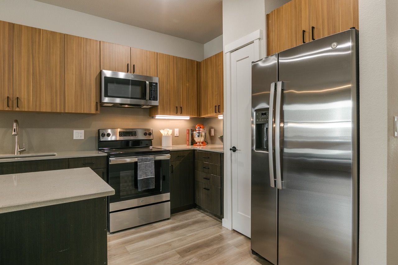 Modern apartment kitchen with stainless steel refrigerator, oven, microwave, and wood cabinets.