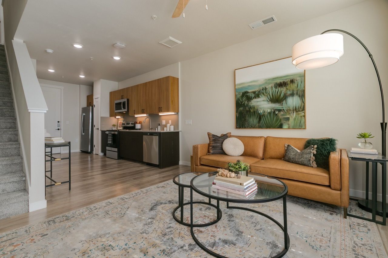 Open-concept living area with tan leather sofa, glass coffee tables, and a modern kitchen.
