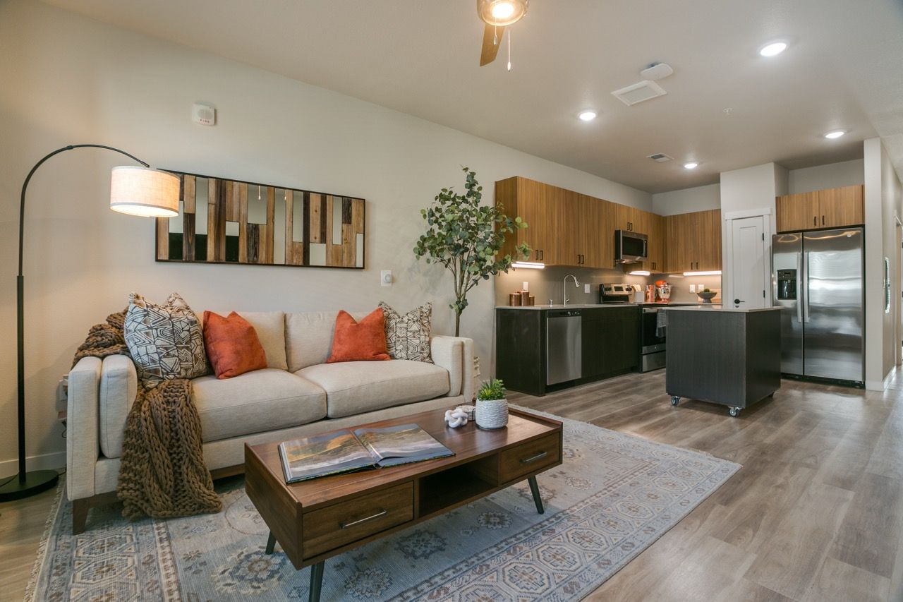 Open-concept living room and kitchen with beige sofa, wood cabinets, and stainless-steel appliances.